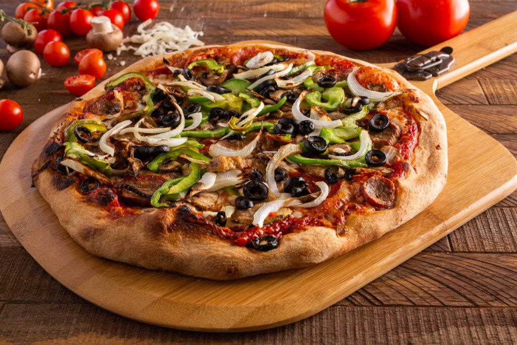 pizza topped with vegetables and meat on pizza peel with vegetables on table